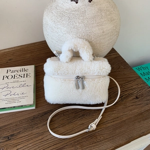 Detail of plush lamb wool mini bag with silver zippers on rustic dark wood table
