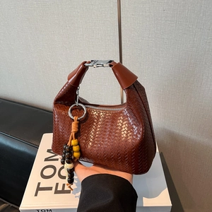 Brown woven hobo bag with metallic handle and wooden bead tassel shown in hand