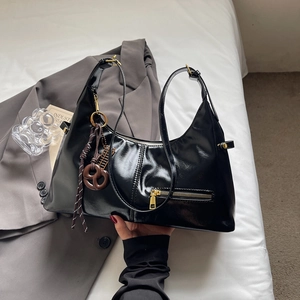 Sac à bandoulière noir brillant avec détails dorés et pendentif marron minimaliste