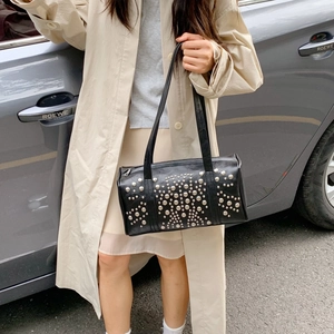 Black leather underarm bag with silver stud patterns shown on shoulder in street style