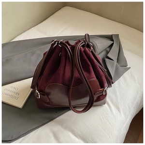 Détail du sac seau bordeaux en daim et cuir avec boucles argentées sur lit blanc