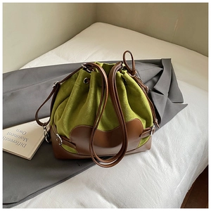 Gros plan d'un sac seau en daim vert avec détails en cuir marron et anneaux argentés