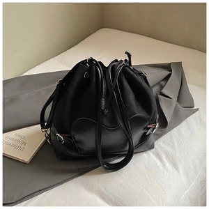 Détail d'un sac seau noir avec cordon et textures mixtes sur un blazer gris