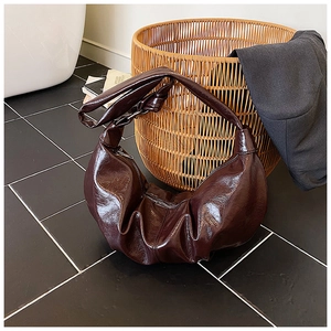 Detail of dark brown wrinkled texture and glossy finish on the minimalist crescent bag