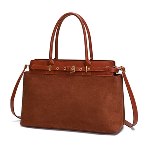 Detail view of large brown tote bag showing mixed leather textures and gold buckle