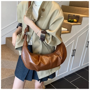 Detail of a dark brown hobo bag featuring pleated faux leather and a decorative knot strap