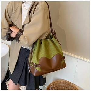 Détail du sac seau en daim vert avec base en cuir marron et écusson en cœur