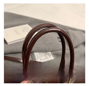 Detail view of smooth dark brown leather handles on a large retro handbag with gold buckle