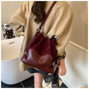 Détail d'un sac seau bordeaux à cordon porté à l'épaule dans un décor intérieur minimaliste