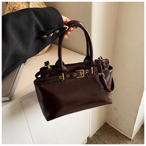 Detail of vintage burgundy leather handbag with gold buckles and model hand styling