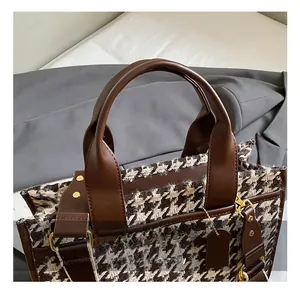 Detail of houndstooth tweed tote bag with brown leather handles and golden hardware