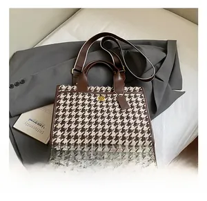 Detail of houndstooth fabric and leather tote bag with gold buckle on grey blazer