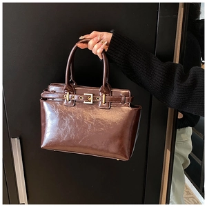Detail of glossy chocolate brown vintage handbag with gold buckle and dual handles