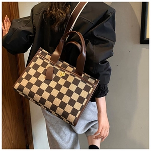 Detail of checkered tote bag with brown leather handles and adjustable woven strap