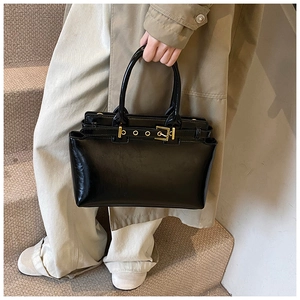 Detail of a black glossy tote bag with gold buckle hardware held by a model in a trench coat