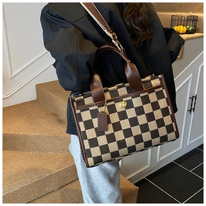 Detail of checkered tote bag with brown leather handles and gold twist lock closure