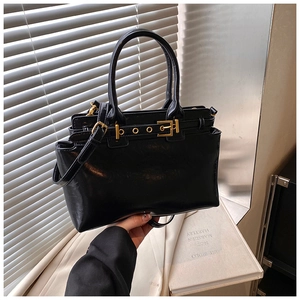 Detail of minimalist black leather tote showing golden buckle and adjustable strap handle