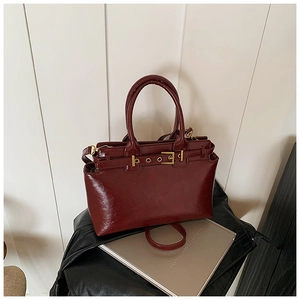 Close-up of elegant burgundy patent leather handbag with gold buckles on a book