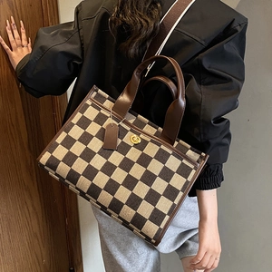 Detail view of checkerboard tote bag with gold metal twist lock and wide shoulder strap