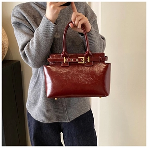 Detail of burgundy glossy oil wax leather handbag with elegant gold metal buckle hardware