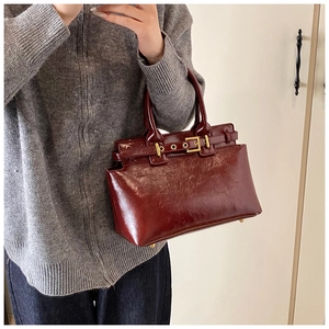 Detailed close-up of glossy reddish-brown vintage handbag with gold metal buckle hardware