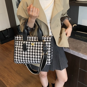 Detail of checkered tote bag with black leather handle and golden metal twist lock closure
