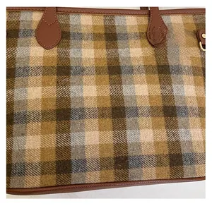 Close-up of wool plaid tote bag with brown leather handle and gold rivet detail