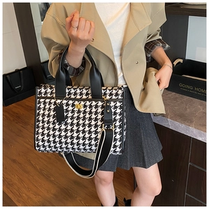 Detail of houndstooth tote bag featuring gold twist lock and striped woven strap