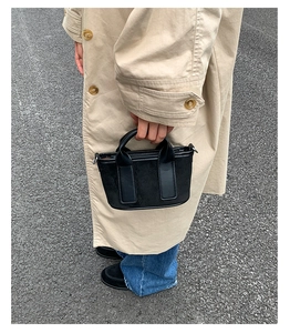Détail d'un mini sac à main en daim noir avec poignées lisses dans un décor de mode urbaine