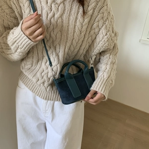 Détail d'un mini sac bandoulière en daim bleu foncé avec poignée en cuir vert