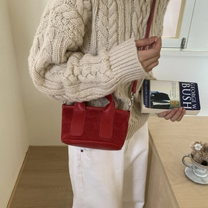 Détail du mini sac vintage rouge en daim et cuir porté sur un pull en maille beige