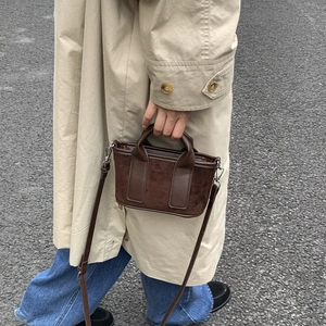 Détail d'un sac bandoulière en toile marron avec poignées en cuir sur fond de goudron