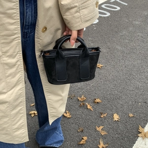 Sac à main noir chic en toile et cuir porté par un mannequin en trench-coat