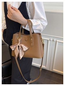 Detail of brown litchi pattern handbag featuring elegant silk scarf and gold hardware