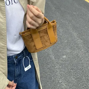 Détail d'un mini sac à main trapèze en daim marron et cuir tenu à la main