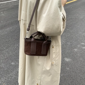 Détail du sac cabas en toile de suède marron porté avec un trench-coat beige chic