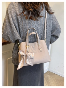 Detail view of beige pebbled leather handbag with decorative printed silk scarf on handle
