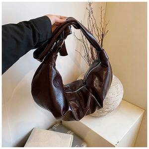 Dark brown pleated croissant bag with glossy finish and knot handle shown by model