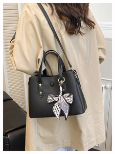 Close-up of black litchi leather handbag with decorative silk scarf and gold studs
