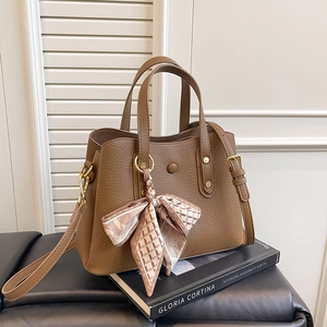 Close-up of brown litchi grain leather handbag with silk scarf on a luxury stool
