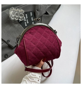 Macro detail of wine red quilted shell bag with metallic kiss-lock closure and suede texture