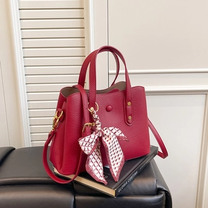 Detail of red pebbled leather handbag with decorative silk scarf and gold hardware