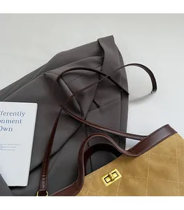 Detail of tan suede bucket bag featuring quilted stitching and golden metal twist lock
