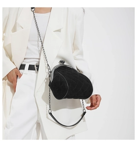 Close-up of black quilted shell bag with metal chain strap on white blazer outfit
