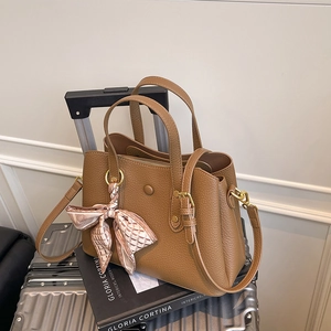 Close-up of brown lychee grain leather handbag with decorative silk scarf and dual handles