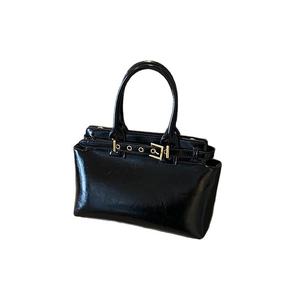 Retro black glossy patent leather handbag with gold buckle and top handle on white background