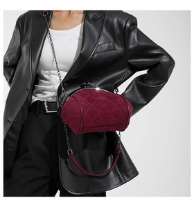 Close-up of quilted burgundy suede crossbody bag with metal chain strap on model