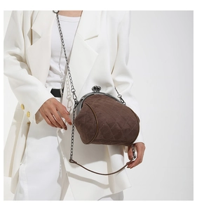 Model wearing dark brown quilted kiss-lock bag with metal chain strap and white suit