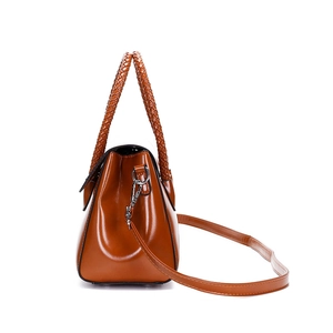 Detail view of brown glossy leather handbag with woven handle and adjustable strap