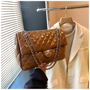 Detail of a dark brown quilted chain bag with a glossy finish and silver turn-lock clasp